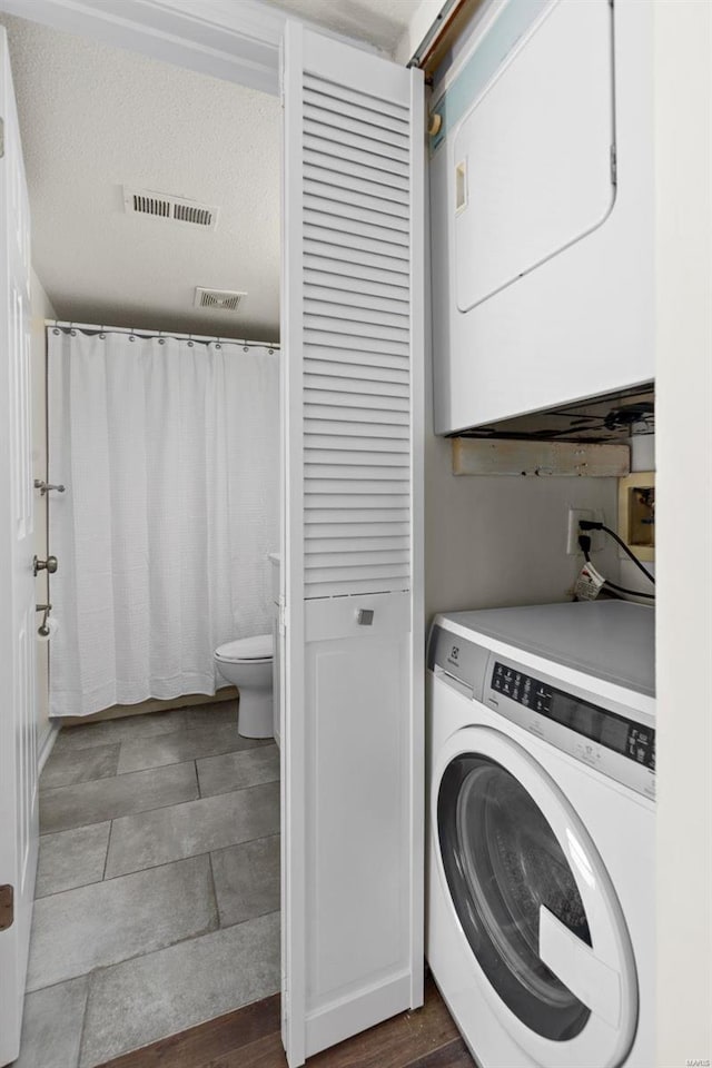 clothes washing area featuring laundry area, visible vents, stacked washer and clothes dryer, and a textured ceiling