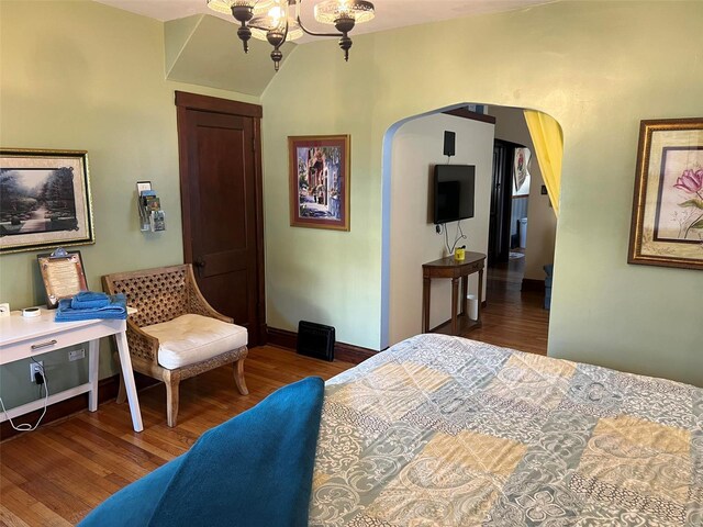 bedroom with arched walkways, a notable chandelier, baseboards, and wood finished floors