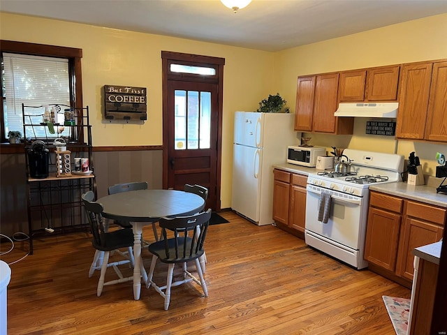 kitchen featuring white appliances, light wood-style flooring, under cabinet range hood, and brown cabinetry