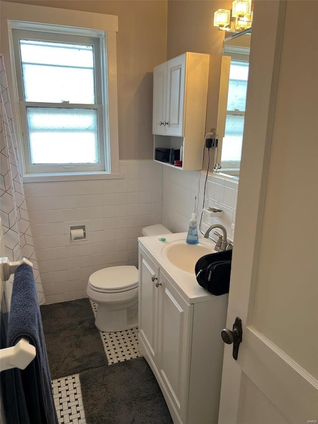 bathroom with wainscoting, toilet, tile patterned floors, vanity, and tile walls