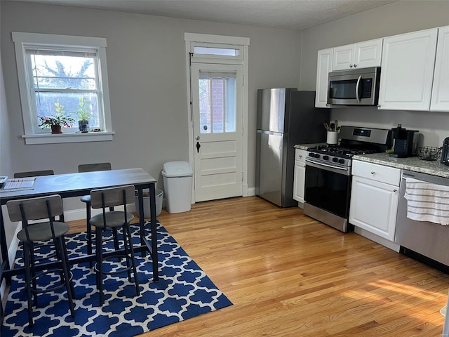 kitchen featuring appliances with stainless steel finishes, white cabinets, light wood-style flooring, and a textured ceiling