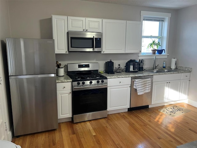 kitchen featuring stainless steel appliances, light wood-type flooring, white cabinets, and a sink