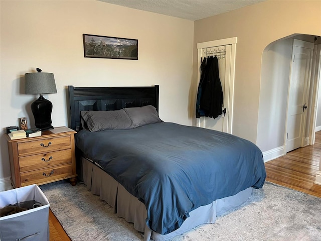 bedroom with arched walkways, wood finished floors, baseboards, a closet, and a glass covered fireplace