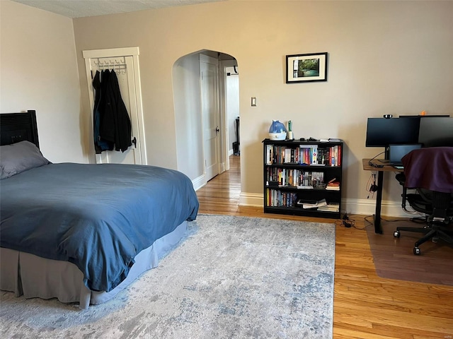 bedroom featuring baseboards, a closet, arched walkways, and wood finished floors