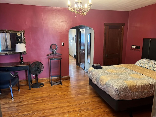 bedroom with arched walkways, a notable chandelier, baseboards, and wood finished floors