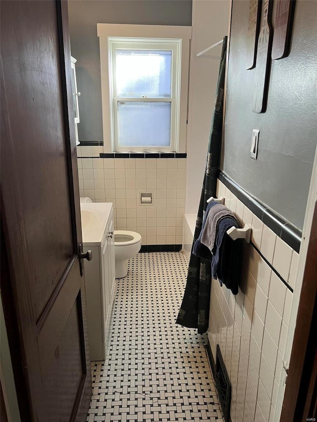 full bath with toilet, a wainscoted wall, tile walls, and vanity