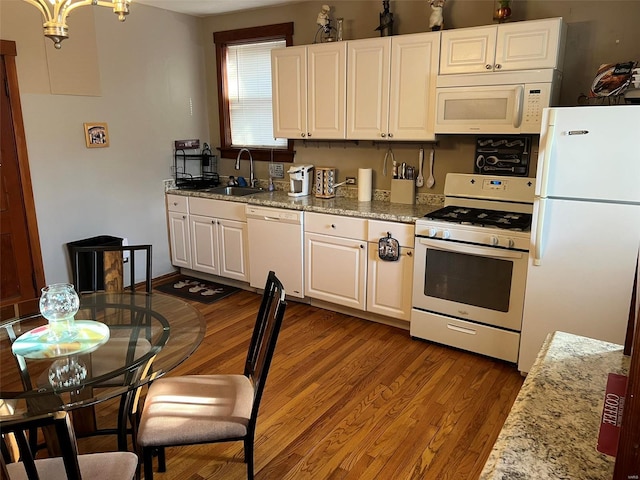 kitchen featuring white appliances, wood finished floors, a sink, white cabinets, and light stone countertops