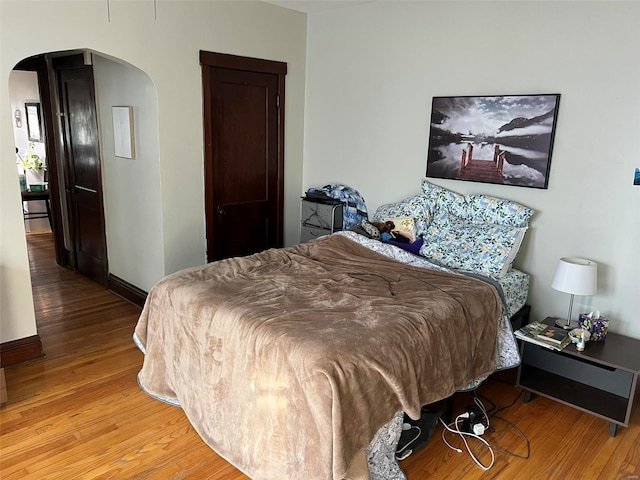 bedroom with baseboards, arched walkways, and wood finished floors