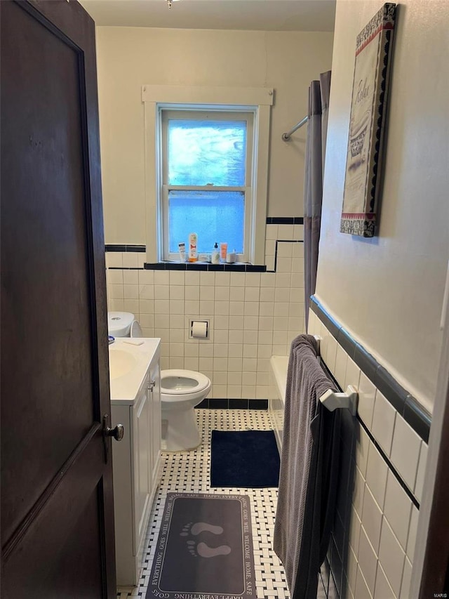 full bath featuring toilet, a wainscoted wall, tile walls, and vanity