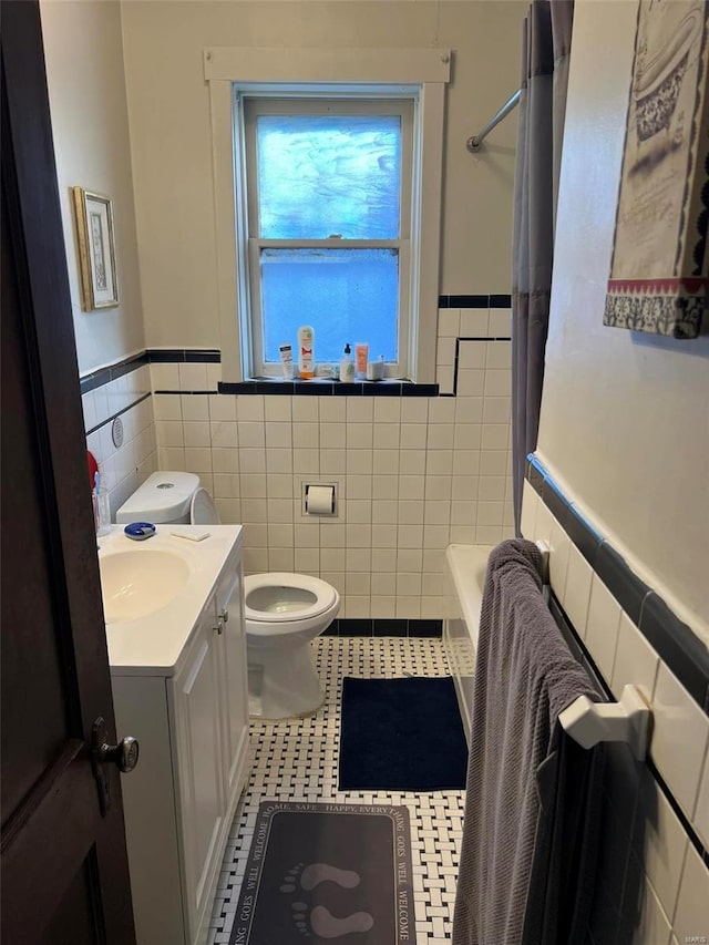 bathroom featuring toilet, a wainscoted wall, tile patterned floors, vanity, and tile walls