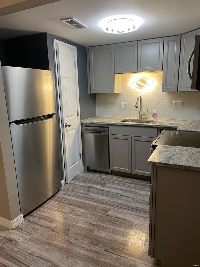 kitchen featuring light wood finished floors, stainless steel appliances, visible vents, gray cabinetry, and a sink