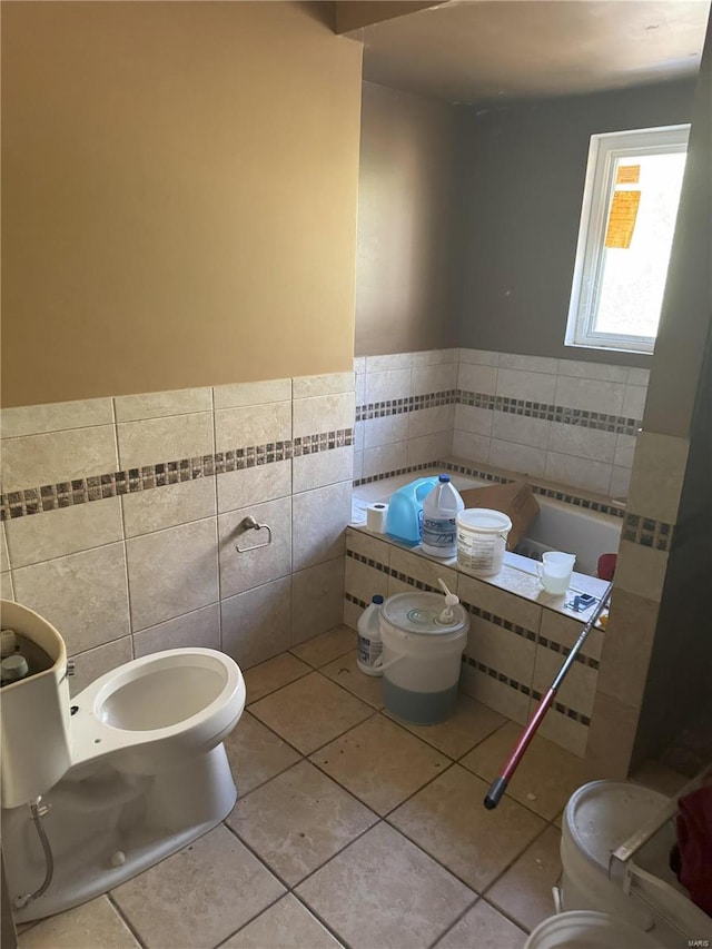 bathroom featuring tile walls, toilet, a wainscoted wall, tile patterned floors, and a bath