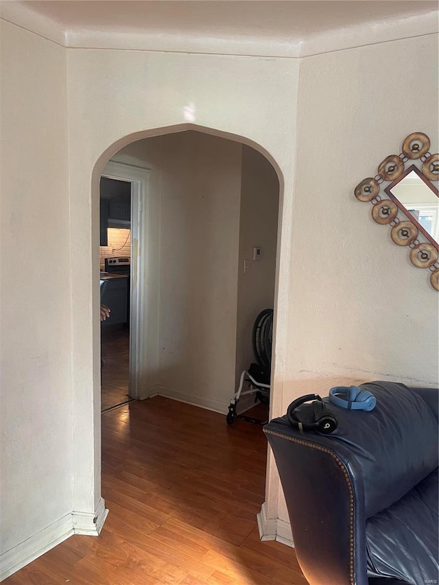 hallway featuring baseboards, arched walkways, and wood finished floors