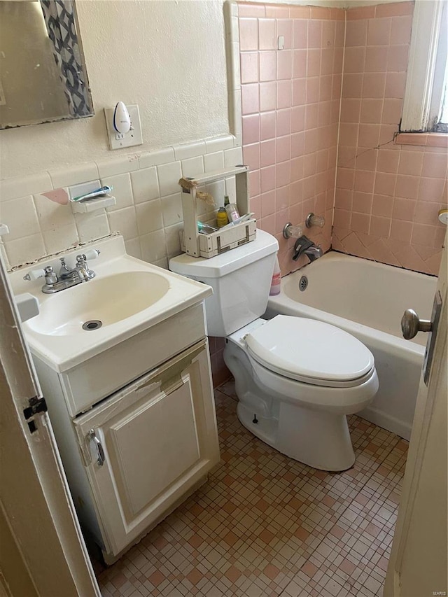 full bath with tile walls, shower / bath combination, toilet, wainscoting, and vanity