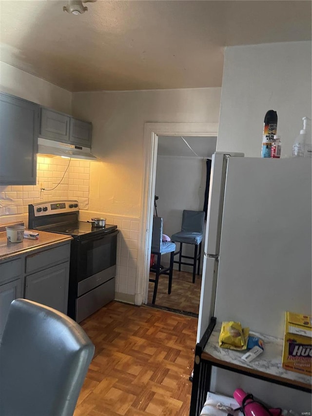 kitchen with gray cabinets, decorative backsplash, freestanding refrigerator, under cabinet range hood, and stainless steel electric range