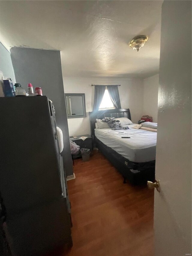 bedroom with freestanding refrigerator and wood finished floors