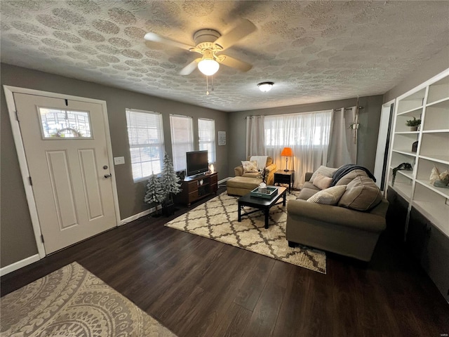 living area featuring a ceiling fan, dark wood-style flooring, a textured ceiling, and baseboards