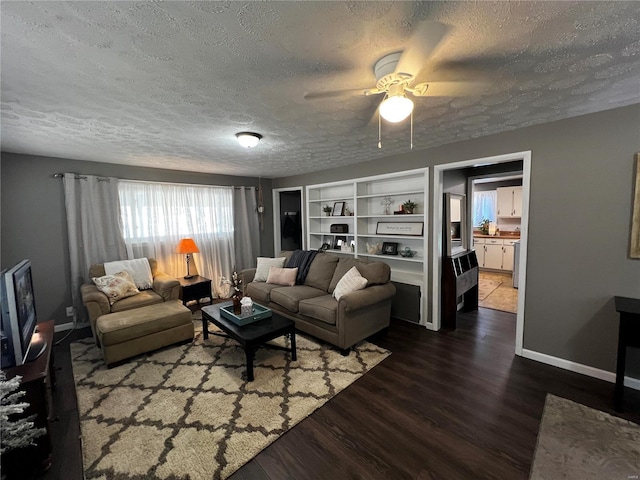 living area featuring built in shelves, dark wood-style flooring, ceiling fan, a textured ceiling, and baseboards