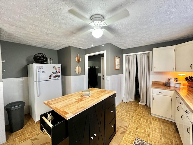 kitchen featuring wainscoting, butcher block counters, freestanding refrigerator, light floors, and tile walls