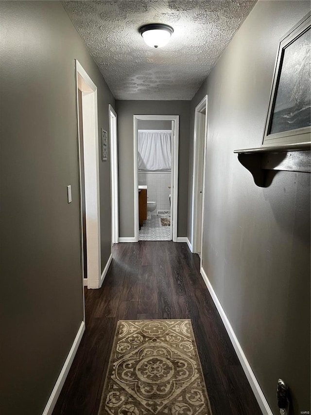 corridor featuring dark wood-type flooring, a textured ceiling, and baseboards