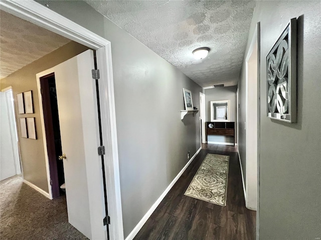 hall featuring visible vents, a textured ceiling, baseboards, and wood finished floors