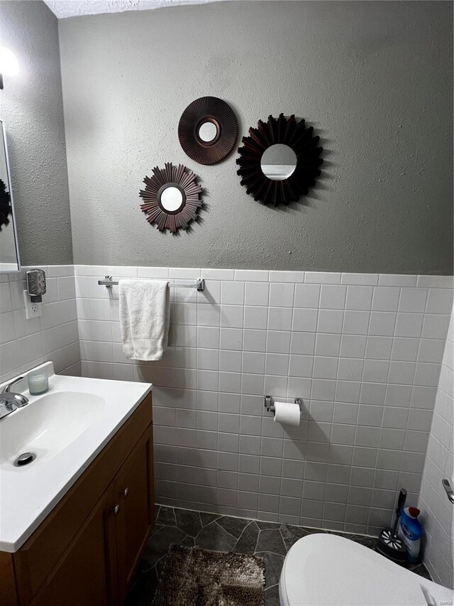 bathroom with wainscoting, tile walls, toilet, and vanity