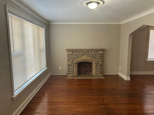 unfurnished living room featuring plenty of natural light, arched walkways, a fireplace, and wood finished floors