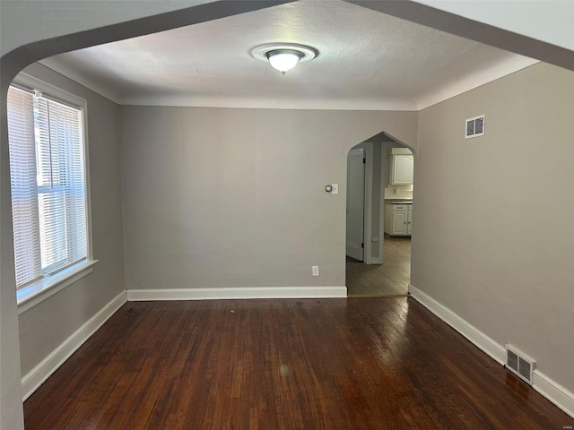 unfurnished room with arched walkways, visible vents, baseboards, and wood finished floors