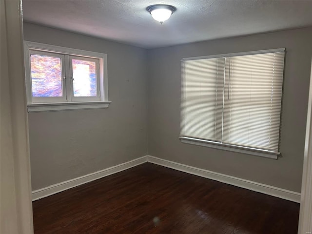 spare room featuring a textured ceiling, baseboards, and dark wood-type flooring