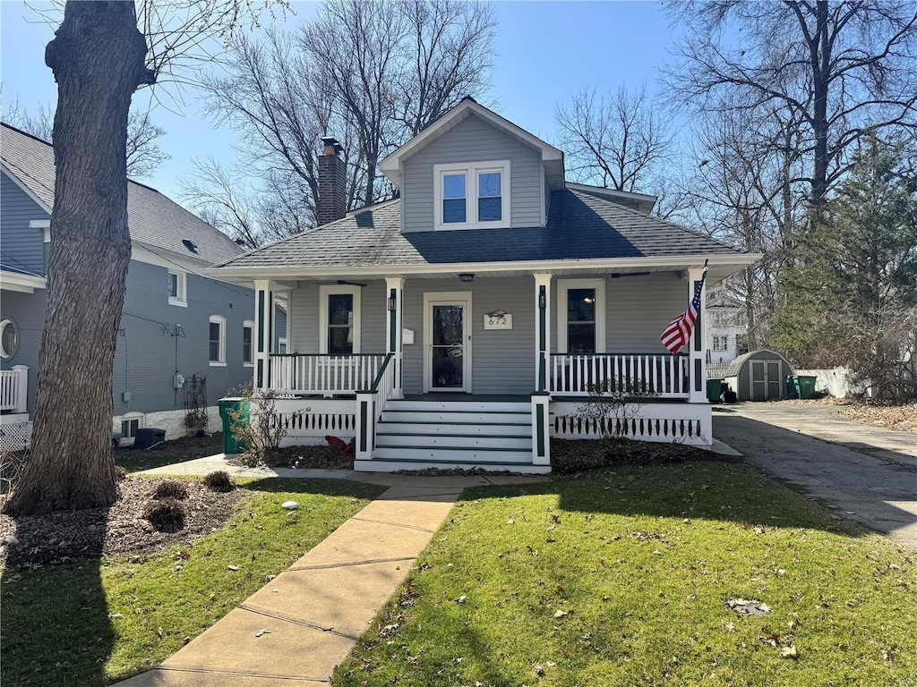 bungalow featuring cooling unit, covered porch, a storage shed, an outdoor structure, and a front lawn