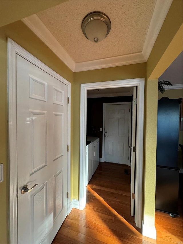 hallway with wood finished floors, a textured ceiling, independent washer and dryer, and ornamental molding