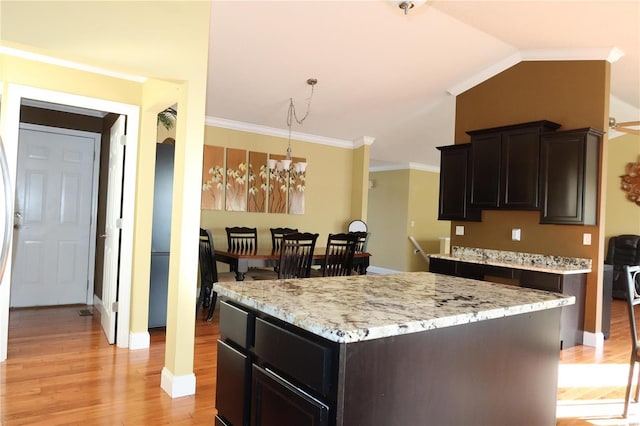 kitchen featuring light stone countertops, light wood finished floors, lofted ceiling, an inviting chandelier, and crown molding