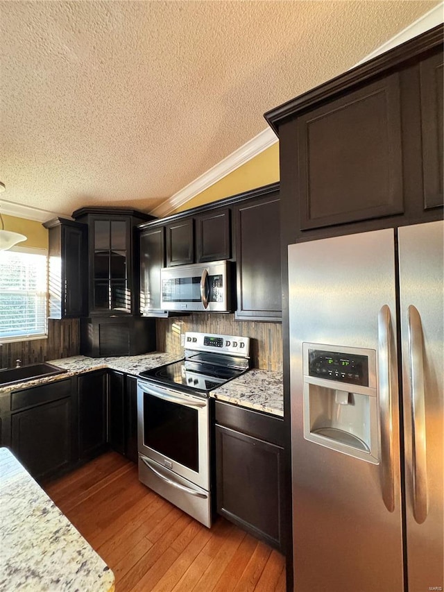 kitchen featuring a sink, ornamental molding, vaulted ceiling, stainless steel appliances, and light wood-type flooring