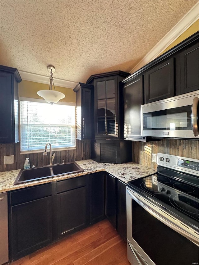 kitchen featuring a sink, a textured ceiling, wood finished floors, stainless steel appliances, and crown molding