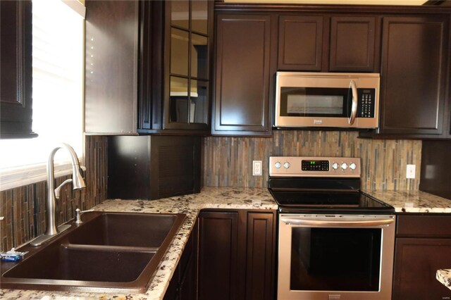 kitchen with a sink, backsplash, stainless steel appliances, dark brown cabinetry, and glass insert cabinets