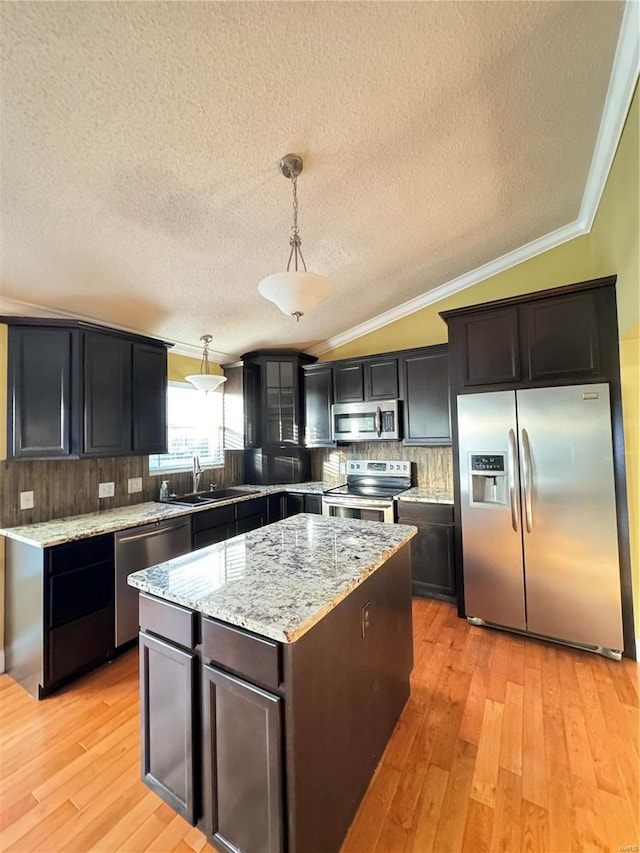 kitchen with lofted ceiling, ornamental molding, a sink, appliances with stainless steel finishes, and a center island