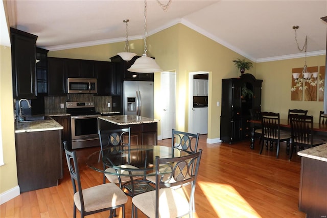 kitchen with a sink, appliances with stainless steel finishes, light wood finished floors, decorative backsplash, and lofted ceiling