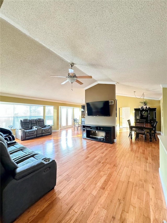 living room with a ceiling fan, lofted ceiling, ornamental molding, light wood-style floors, and a textured ceiling