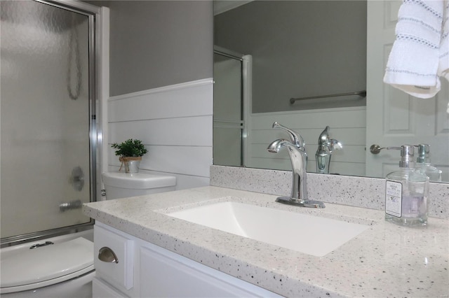 full bath featuring combined bath / shower with glass door, a wainscoted wall, toilet, and vanity