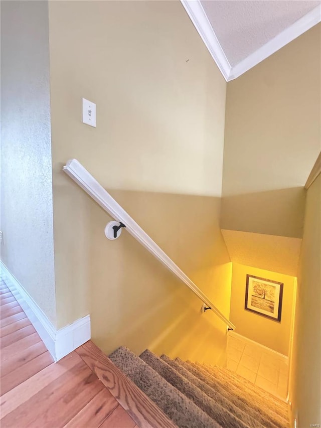 stairway with a textured ceiling, wood finished floors, baseboards, and ornamental molding