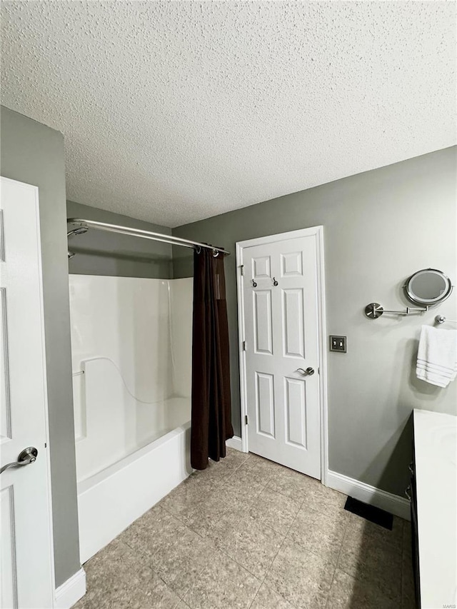 bathroom with a textured ceiling, shower / bath combo with shower curtain, and baseboards