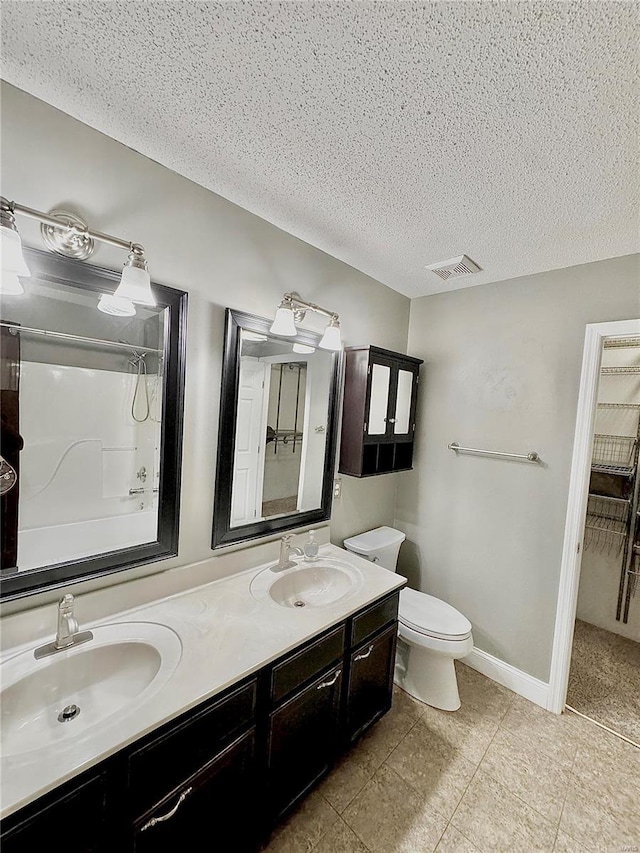 full bath featuring double vanity, toilet, a textured ceiling, and a sink