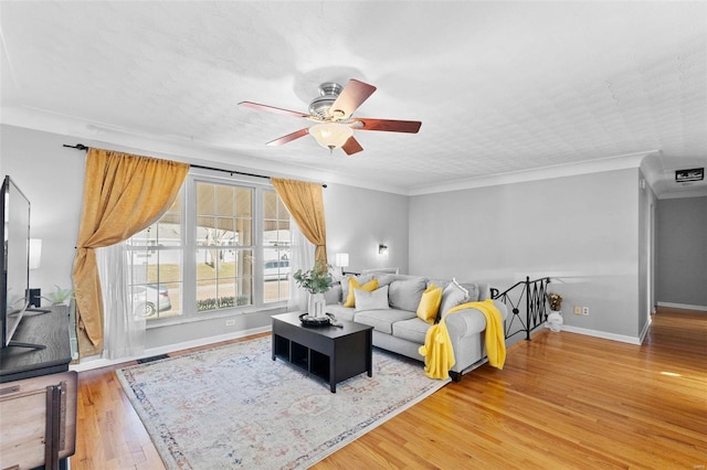 living room with wood finished floors, visible vents, baseboards, ceiling fan, and crown molding