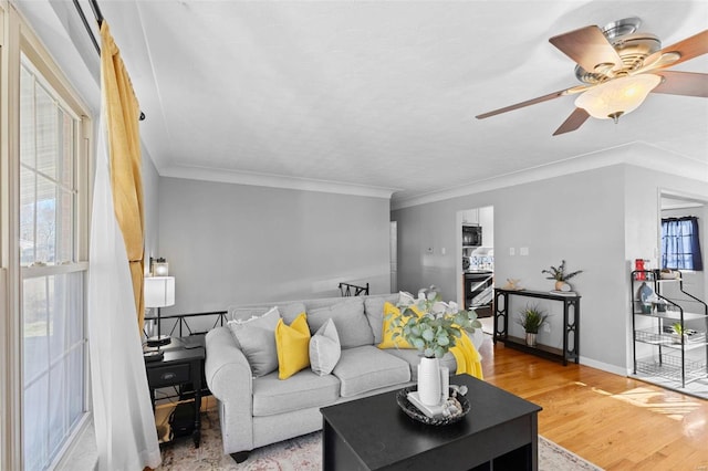 living area with ornamental molding, a ceiling fan, baseboards, and wood finished floors