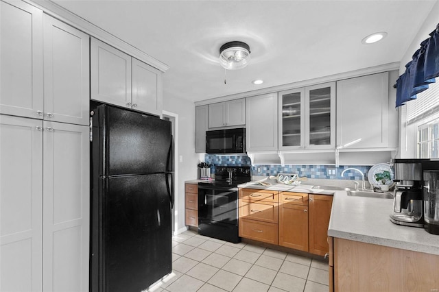 kitchen featuring light tile patterned floors, decorative backsplash, black appliances, light countertops, and glass insert cabinets