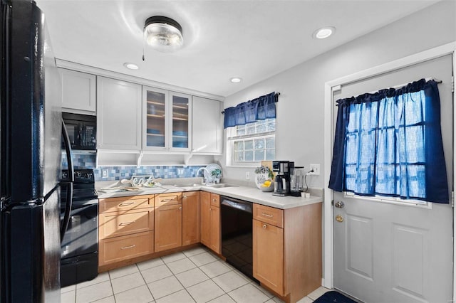 kitchen featuring black appliances, a sink, light countertops, light tile patterned floors, and glass insert cabinets