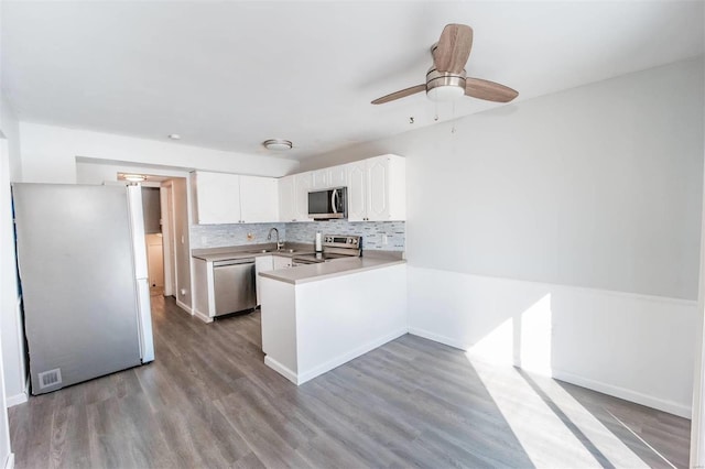 kitchen with stainless steel appliances, light countertops, backsplash, white cabinets, and a peninsula