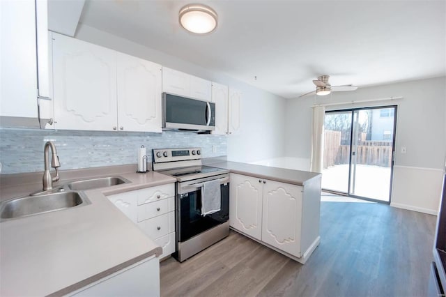 kitchen with a peninsula, a sink, white cabinets, appliances with stainless steel finishes, and light wood finished floors