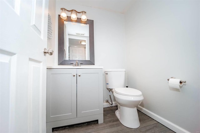 half bath with visible vents, toilet, vanity, wood finished floors, and baseboards