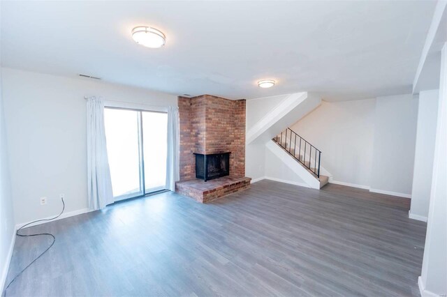 unfurnished living room with baseboards, visible vents, wood finished floors, stairs, and a brick fireplace